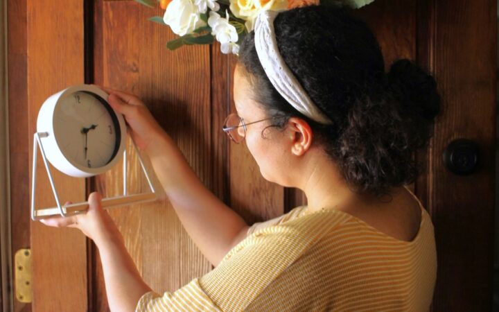 a woman holding a clock in her hands wearing a head band and yellow shirt