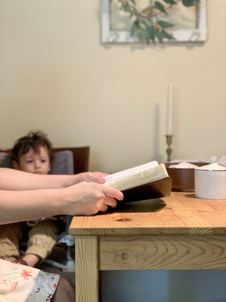 baby eating and mom reading the Bible at the table